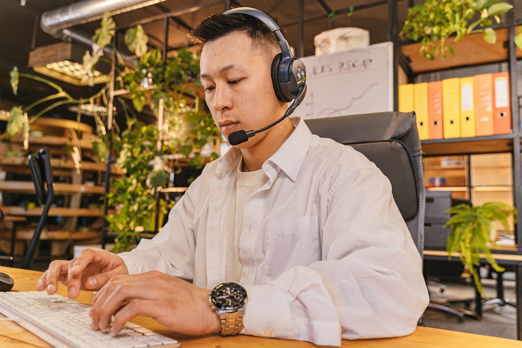 Professional Asian male working at desk with headset in office setting.