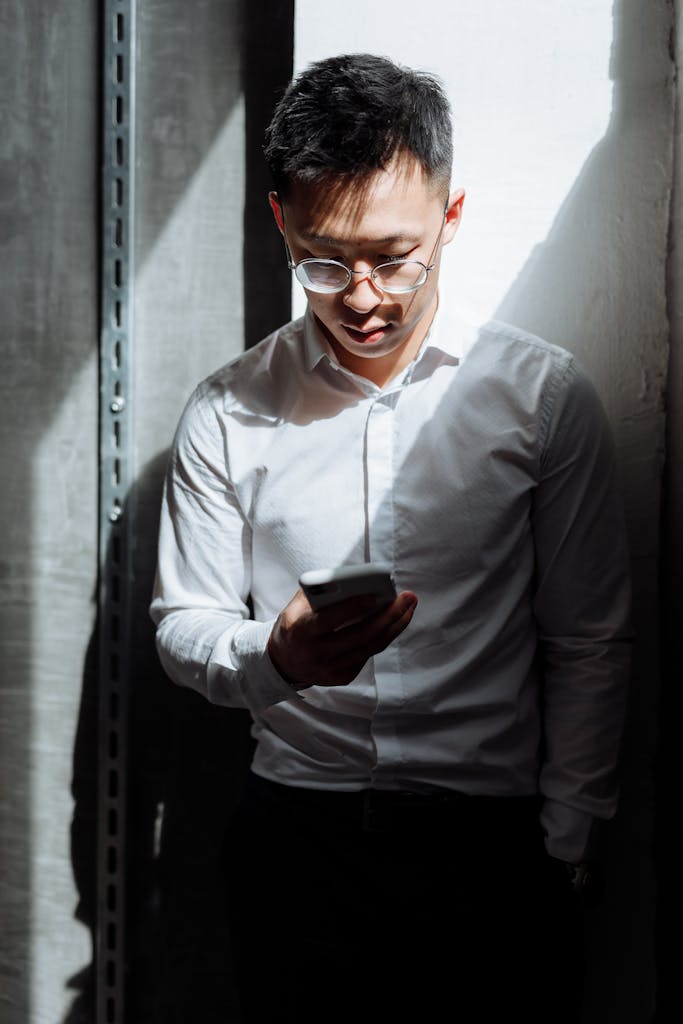 Young Asian businessman in professional attire using smartphone in office setting.